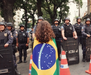 Polizia per le strade di Rio de Janeiro e una  manifestante avvolta dalla bandiera brasiliana